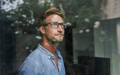 Een man met bril kijkt uit het raam