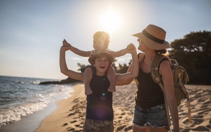 Eine Mutter und ihre zwei Kinder gehen lachend am Strand spazieren.