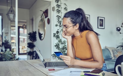 Eine brünette Frau in einem orangenen Top sitzt am Schreibtisch und kümmert sich um ihre Altersvorsorge