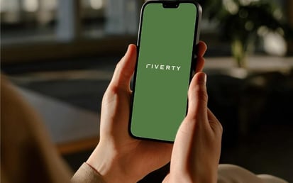 Riverty-Logo auf dem Handy-Display, gehalten in beiden Händen