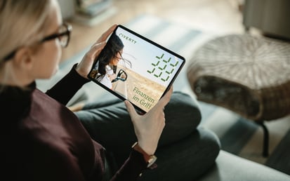 Eine blonde Frau sitzt auf dem Sofa und schaut sich auf ihrem Tablet den Riverty Finanzplaner.