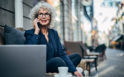En kvinde med briller sidder og taler i smartphone på en café