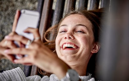 Lachende vrouw beheert haar financiën met Riverty Back in Flow op haar telefoon