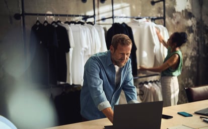 En mand står ved en laptop i en tøjbutik