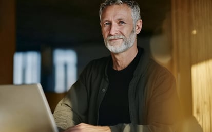 Mann, am Schreibtisch sitzend, mit seinem Laptop vor sich.