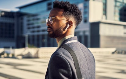 En mand med guldfarvet brillestel og hvide høretelefoner står på gaden