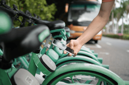 Es ist eine Reihe von E-Bikes sichtbar, sowie eine Person, die dort mit dem Smartphone einen QR-Code scannt.