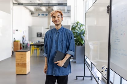 young man holding his laptop while smiling into the camera