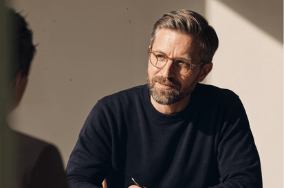 Ein Mann mit Brille hält einen Stift in der Hand und spricht mit einer anderen Person.