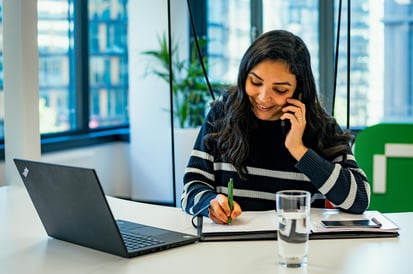 Eine Frau im hellen Riverty Büro, telefoniert und schreibt 