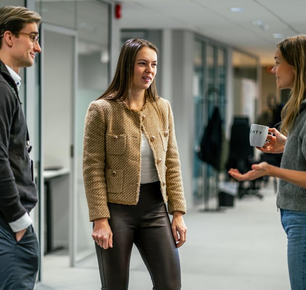 Three Riverty colleagues the oslo office hallway having a casual conversation, with one holding a coffee mug.