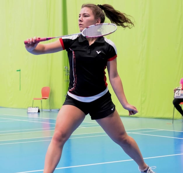 Thelma in an indoor badminton court, about to hit the shuttlecock.