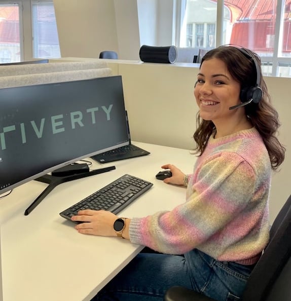 Thelma seated at her desk with 'Riverty' displayed on the computer screen.