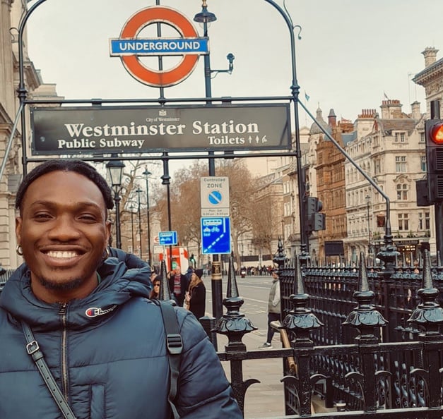 Timothy ist warm angezogen und steht vor einem Schild der 'Westminster Station'.