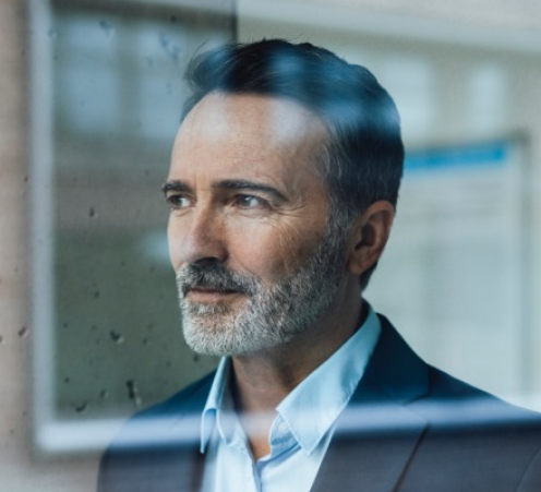 Geschäftsmann im Anzug mit grauem Bart blickt aus einem Fenster, Nahaufnahme