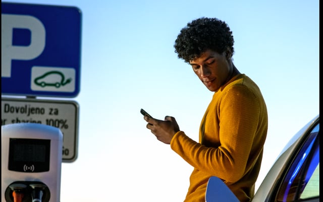 Ein Mann lehnt am Auto und parkt per E-Station