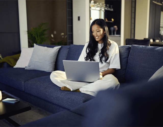 Billede af en kvinde der sidder på sofaen og surfer på sin bærbare computer.
