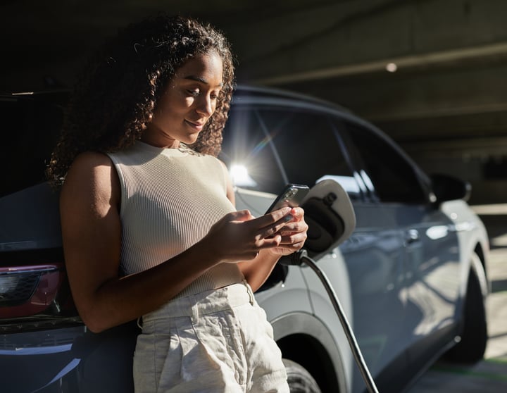 Eine Frau lehnt mit einem Mobiltelefon in der Hand an ihrem Auto