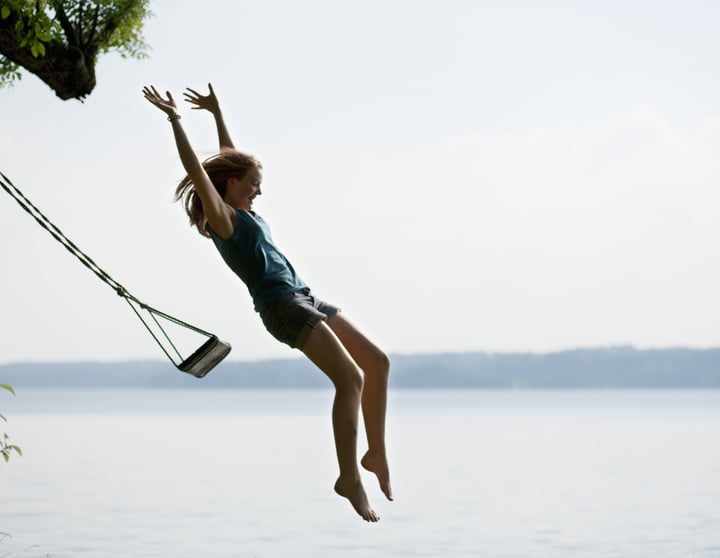 Eine junge Frau springt mit erhobenen Armen von einer schwingenden Schaukel in einen See