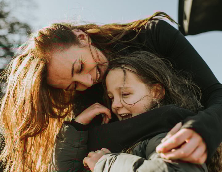 Eine Mutter umarmt ihre Tochter von hinten und beide haben ein Strahlen im Gesicht