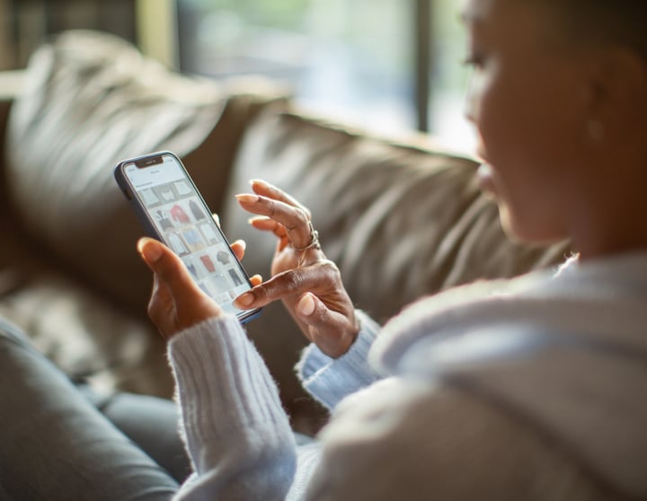 Een vrouw zit op de bank met een telefoon in haar hand