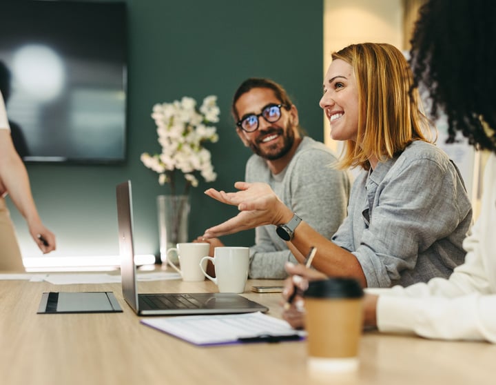 Vier junge Männer und Frauen stehen und sitzen an einem Tisch, trinken Kaffee und quatschen über ihre Finanzen und ihre Zukunft