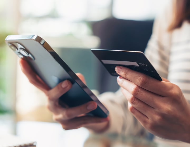 Vrouw heeft een telefoon in haar linkerhand en een creditcard in haar andere hand