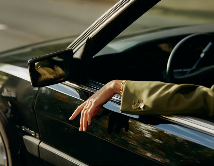 Hand einer Frau, die ihre Hand aus einem grünen Auto hält und einen grünen Anzug trägt.