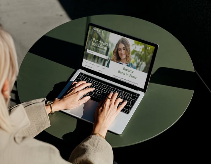Geöffnetes Macbook, flow.riverty.com ist im Browser geöffnet, während eine Frau sich dort einloggt.