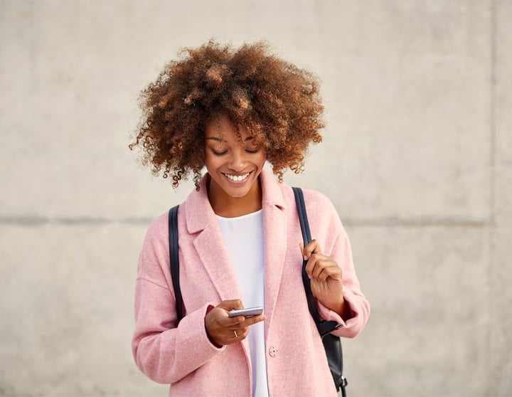 Eine junge Frau in einem rosa Shirt schaut lächelnd auf ihr Handy