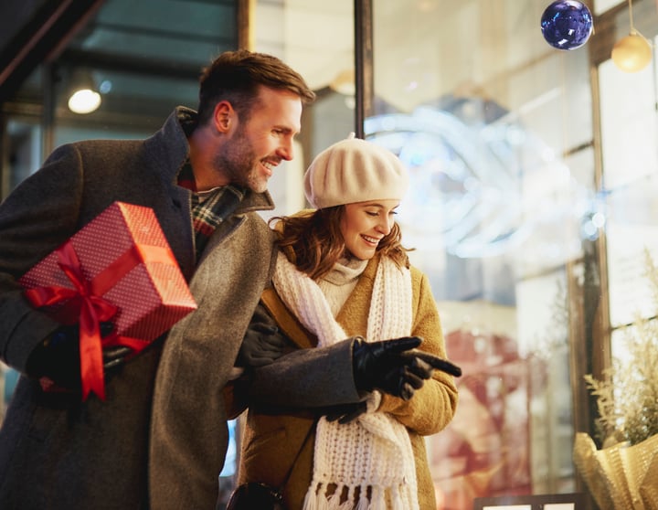Eine junge Frau und ein junger Mann stehen am Maria Empfängnis Tag vor einem Schaufenster und machen eine Shoppingtour