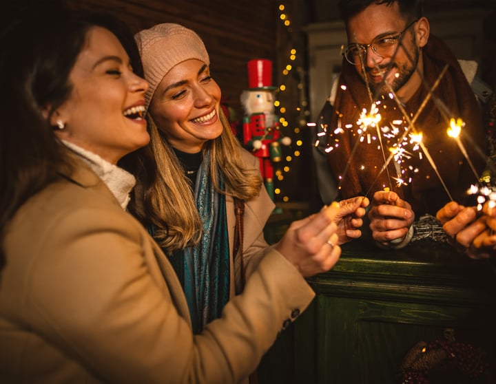 Eine Freundesgruppe steht draußen und feiert mit Sekt und Wunderkerzen in das neue Jahr