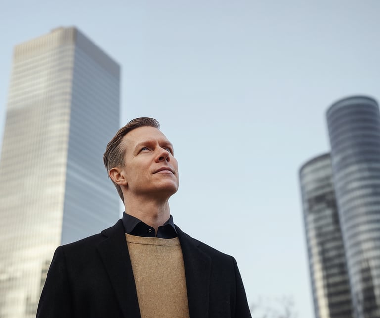 Man in business attire looking upward in front of modern high-rise buildings