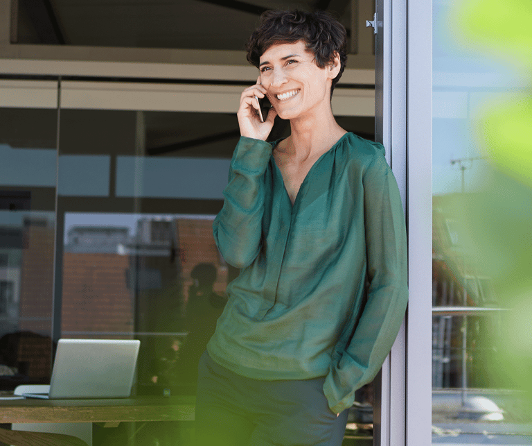 eine Frau in einem Büro in grüner Bluse, die telefoniert und aus dem Fenster schaut.