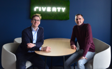 Vertreter von Riverty und Sinpex lächeln mit einem Riverty-Logo hinter sich
