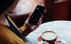 Person mit Handy und Kaffee in der Hand