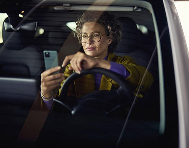 Kvinna i en parkerad bil tittar i mobiltelefon