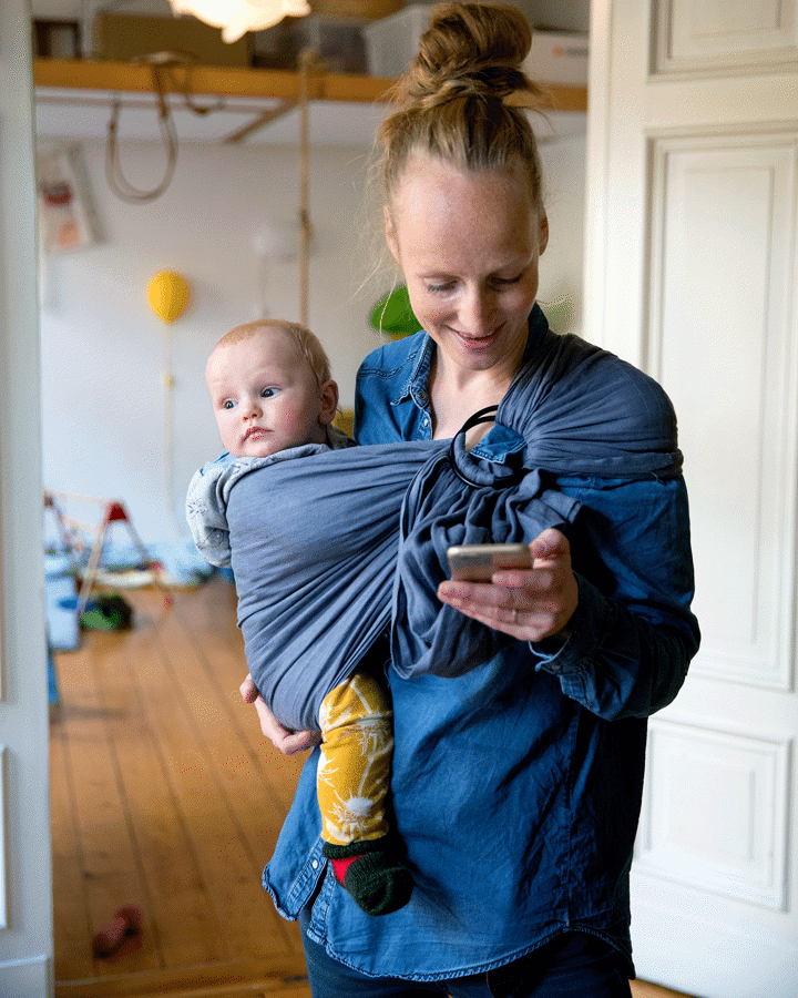 En kvinde med et barn i en slynge tjekker sin mobiltelefon