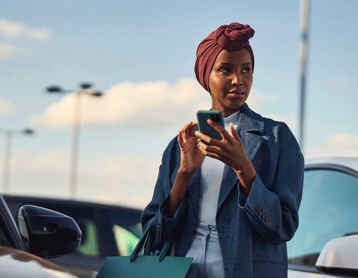 En kvinna står vid parkeringsplats med en mobil i handen