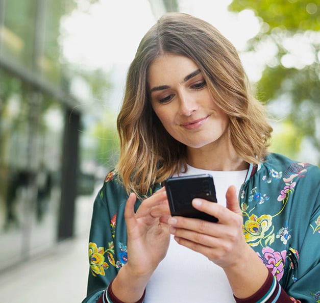 Junge, lächelnde Frau in der Stadt mit einem Smartphone in der Hand