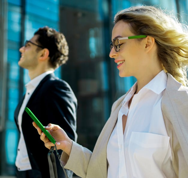 Two co-workers walking alongside, one of them is checking her mobile phone.