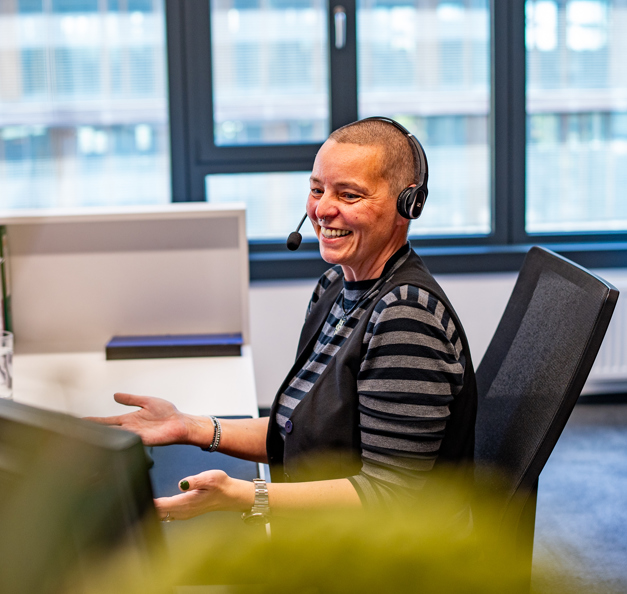 Frau sitzt am Schreibtisch und telefoniert via Headset