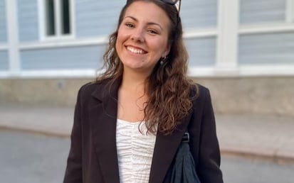 Ein Bild von Thelma vor einem Haus. Sie hat dunkle Haare und trägt eine Sonnenbrille.