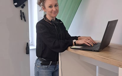 Antonina steht in einem Besprechungsraum vor ihrem Laptop. Ihre Haare sind zu einem hohen Pferdeschwanz gebunden