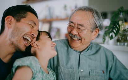 Ein junges Mädchen sitzt auf dem Schoß von ihrem Vater lacht gemeinsam mit ihrem Vater und ihrem Großvater
