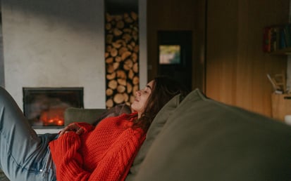 Eine junge Frau sitzt gemütlich auf ihrem grünen Sofa und hat ihre Augen geschlossen
