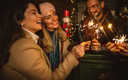 Eine Freundesgruppe steht draußen und feiert mit Sekt und Wunderkerzen in das neue Jahr