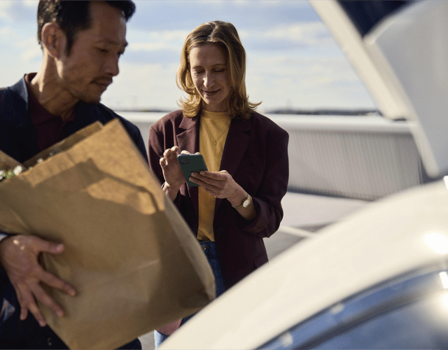 Image of a man and a woman putting groceries into the trunk of their car.